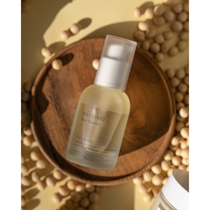 Mixsoon Bean Essence 30 ml eksfolierende essence i frostet glassflaske med pumpe plassert i en treskål med soyabønner.