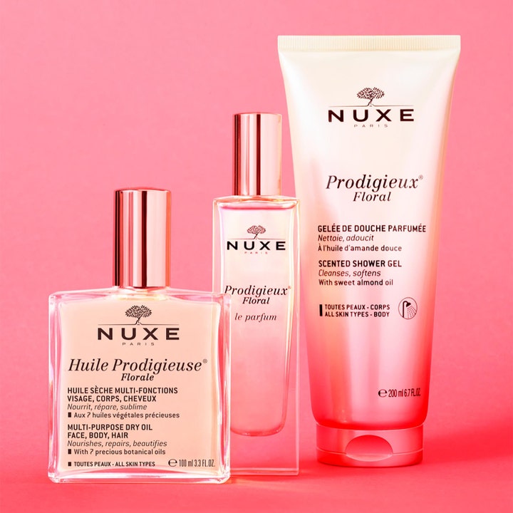 Nuxe Huile Prodigieuse Florale 100 ml pleiende tørrolje i glassflaske med parfyme og dusjgelé på rosa bakgrunn.