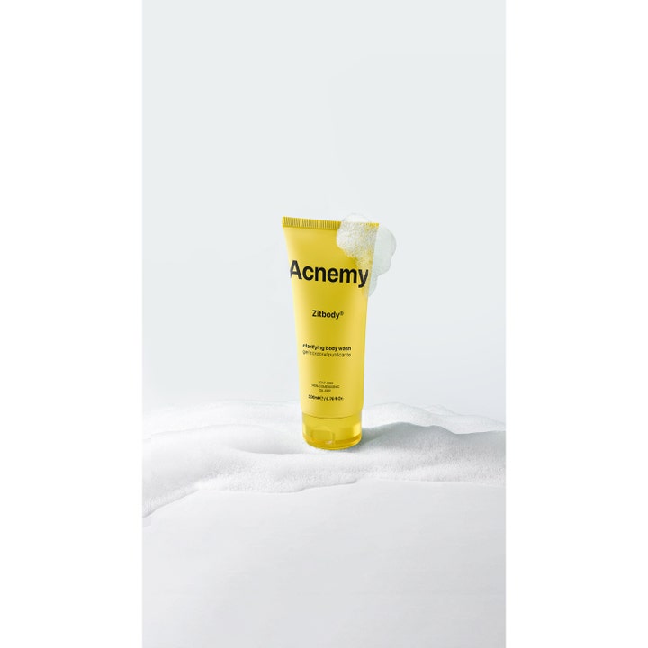 Niche Beauty Lab Acnemy Zitbody 200 ml rensende kroppsvask i gul tube omgitt av hvitt, luftig skum.
