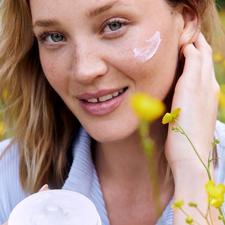 NIVEA Soft 200 ml fuktighetskrem gir myk hud vist på kvinne med hvit krem på kinnet i en sommerlig blomstereng.