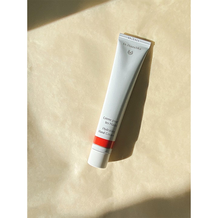 Dr. Hauschka Hand Cream 50 ml fuktighetsgivende håndkrem i hvit tube med rød stripe på en beige overflate.