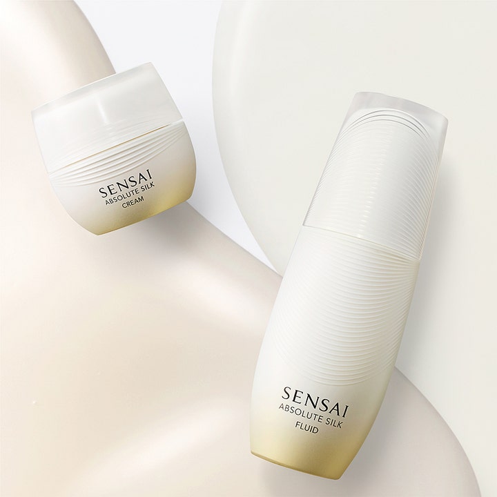 Sensai Absolute Silk Fluid 80 ml fuktighetsgivende ansiktskrem i hvit og gullfarget flaske ved siden av krukke