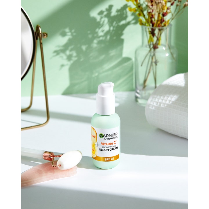 Garnier Skin Active Brightening Serum Cream 50 ml med vitamin C og SPF 25 ved siden av en ansiktsrulle.