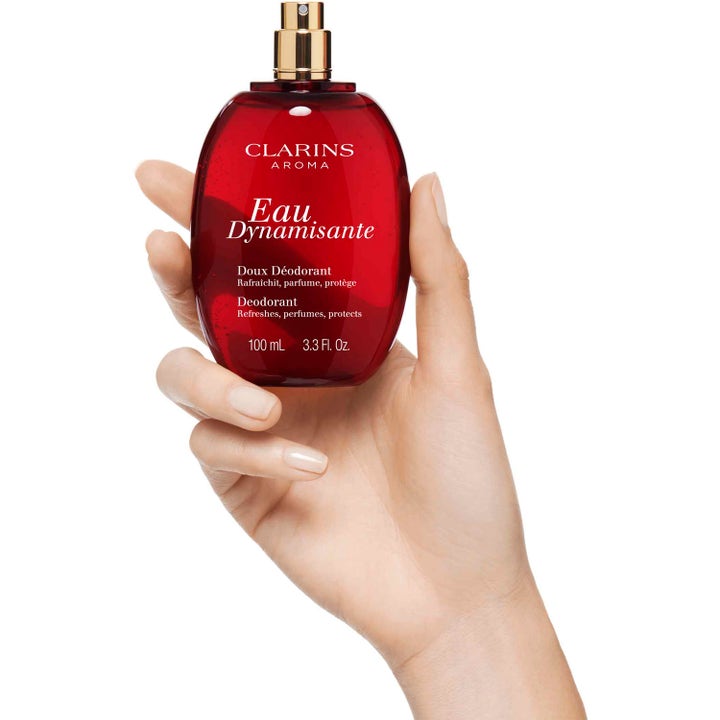 Clarins Eau Dynamisante Deodorant Spray 100 ml beskytter og frisker opp i rød glassflaske som holdes i en hånd.