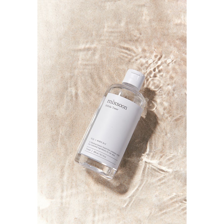 Mixsoon Bifida Toner 300 ml styrkende ansiktsvann i gjennomsiktig flaske på sandbunn dekket av vann.