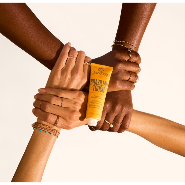 Sol de Janeiro Brazilian Touch Hand Cream 50 ml fuktighetsgivende håndkrem i gul tube holdt av fire hender.