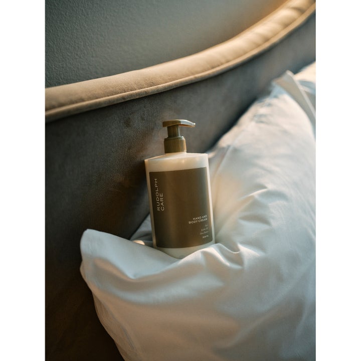 Rudolph Care Hand And Body Cream 500 ml fuktighetsgivende body lotion i pumpeflaske plassert på en hvit pute