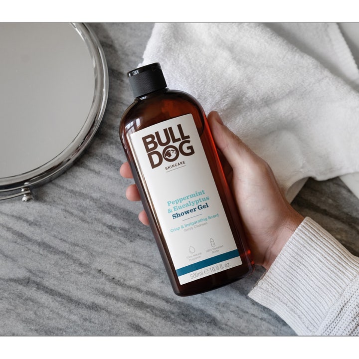 Bulldog Peppermint & Eucalyptus Shower Gel 500 ml holdes i hånden i en baderomssetting ved siden av et speil.