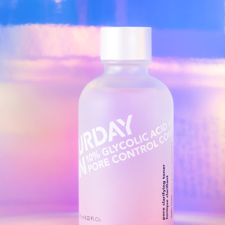 Saturday Skin Pore Clarifying Toner 125 ml med 10% glykolsyre i frostet flaske mot iriserende pastellbakgrunn.