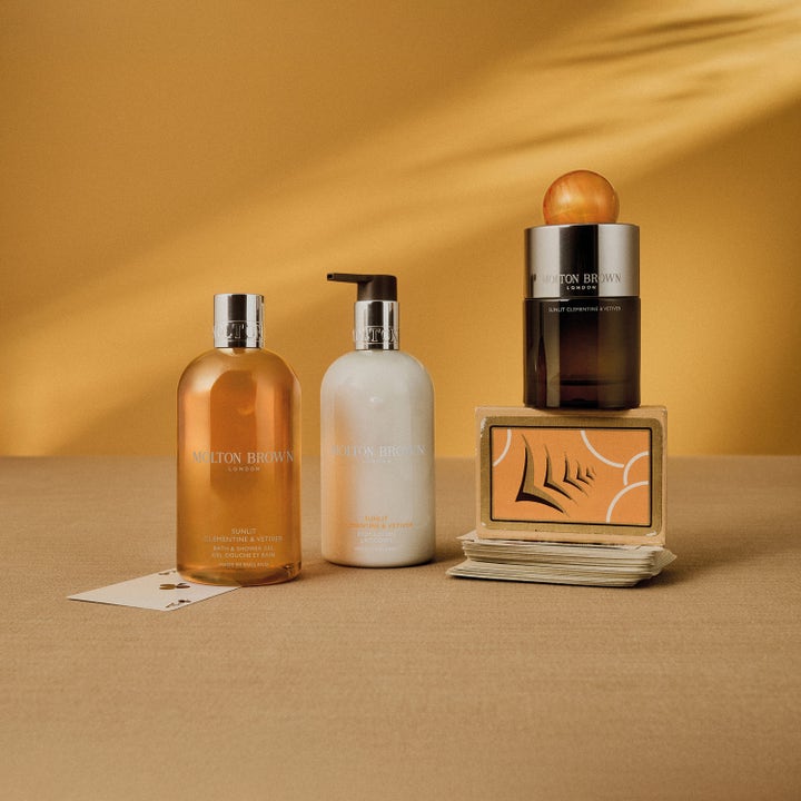 Molton Brown Sunlit Clementine & Vetiver 300 ml fuktighetsgivende body lotion i hvit pumpeflaske i et gyllent miljø.