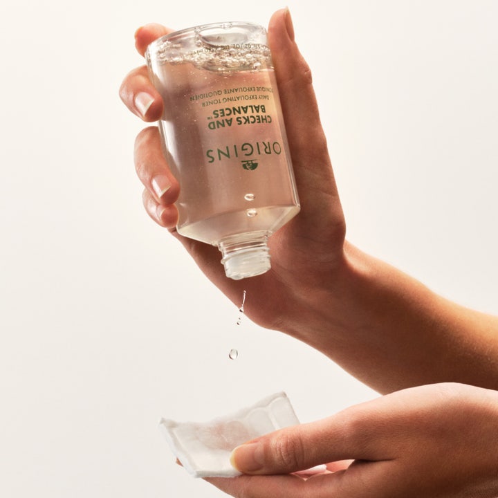Origins Checks and Balances 150 ml eksfolierende toner helles fra den klare flasken over på en hvit bomullspad.