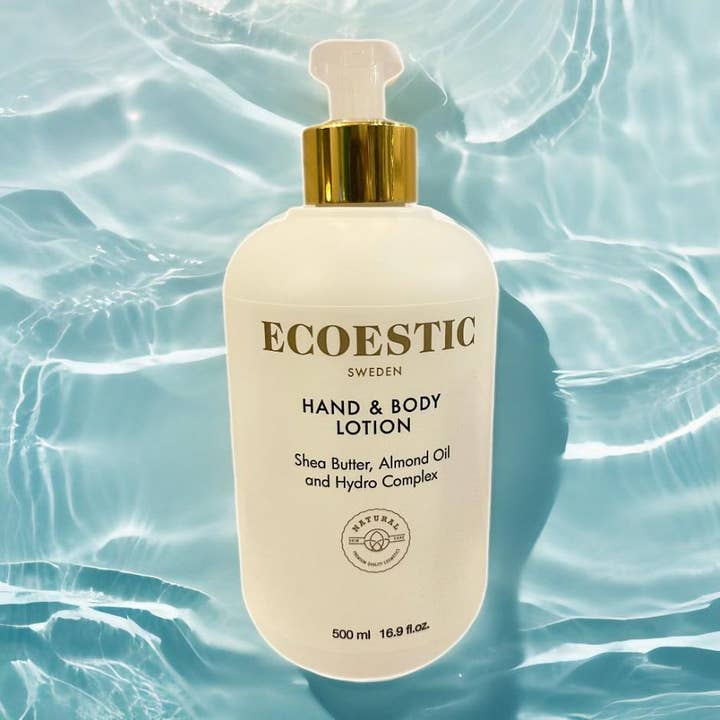 ECOESTIC Hand & Body lotion 500 ml pleiende kroppskrem med sheasmør og mandelolje i hvit flaske mot blått vann