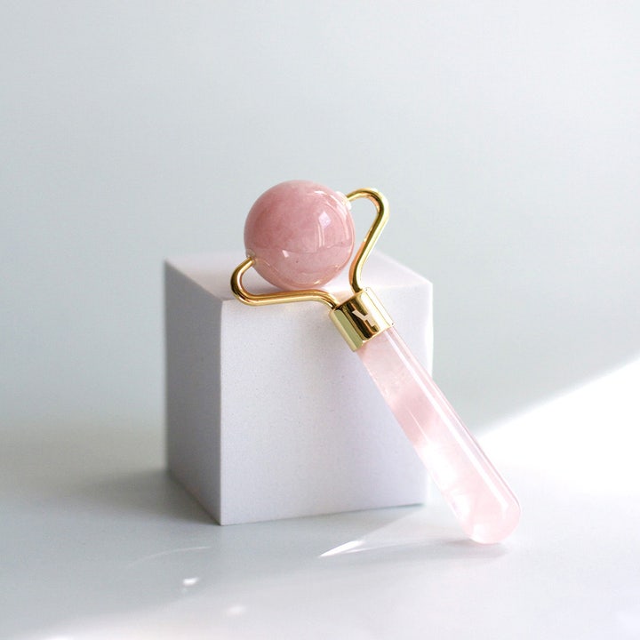 Sense of Youty Eye Massage Roller Rose Quartz øyemassasje i rosa kvarts med gulldetaljer som hviler på en hvit kube