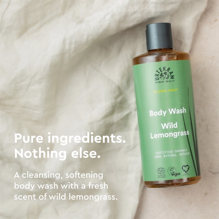 Urtekram Wild Lemongrass Body Wash 500 ml mykgjørende dusjsåpe i grønn flaske plassert på lyst tekstil.