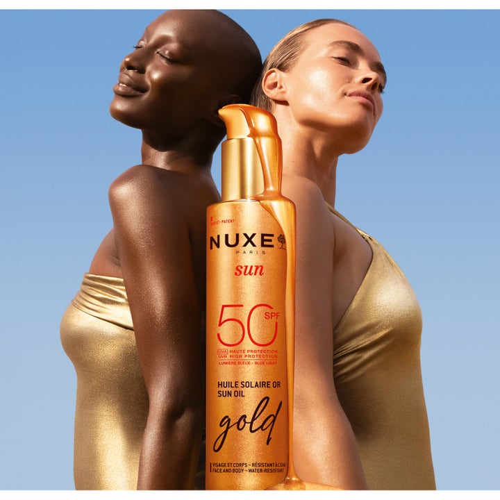 Nuxe Sun Tanning Oil Gold 150 ml sololje SPF 50 gir glødende hud, vist med to kvinner mot blå himmel.