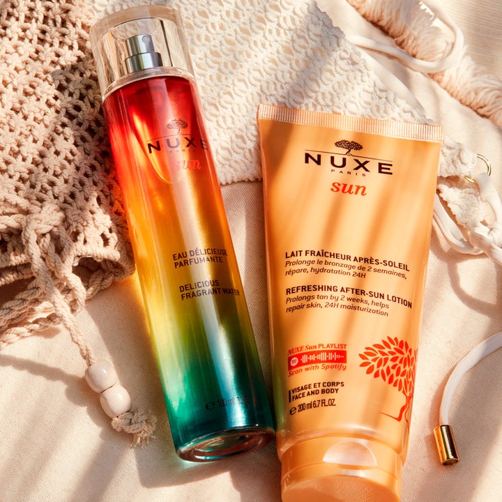 Nuxe Sun Refreshing After Sun Lotion 200 ml beroligende after sun på oransje tube ved siden av fargerik duftspray på strand