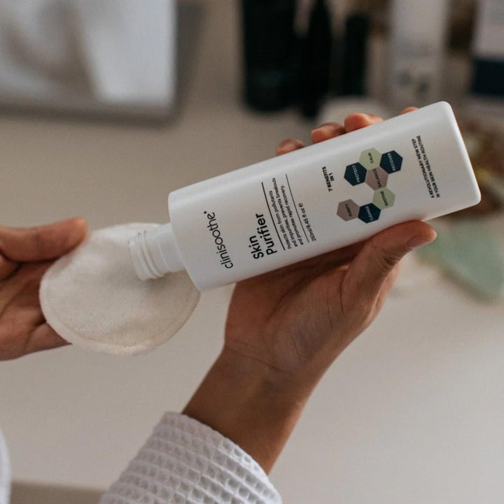 Clinisoothe Skin Purifier 250 ml toner i hvit flaske helles over på en bomullspad for å rense og berolige huden.