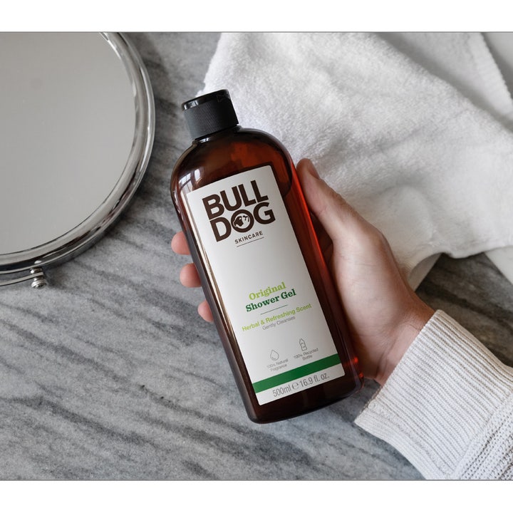 Bulldog Original Shower Gel 500 ml oppfriskende dusjsåpe i brun flaske holdes i en hånd foran et speil og hvitt håndkle.