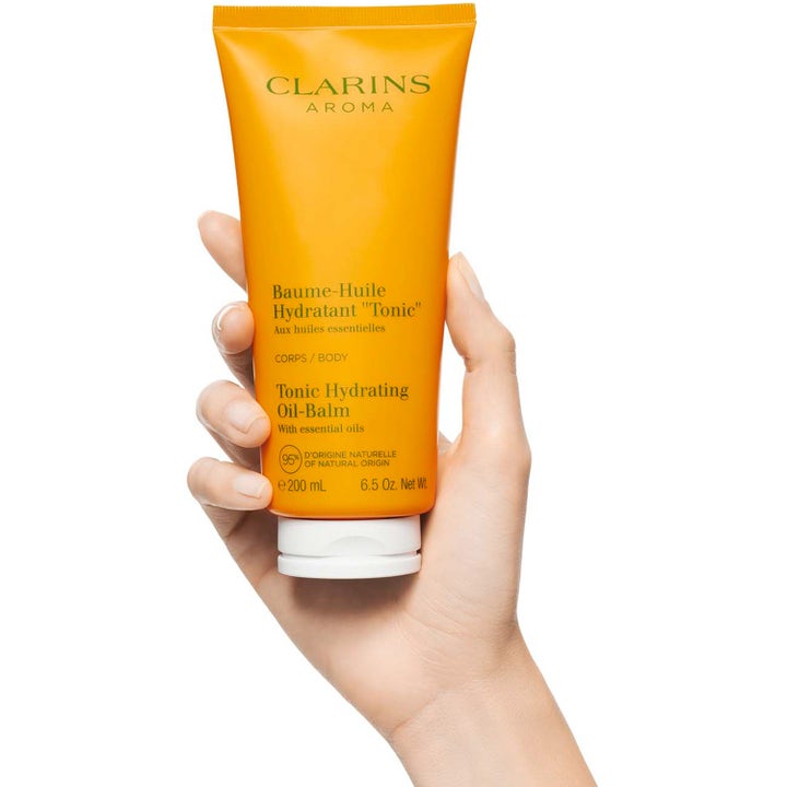 Clarins Hydrating Toning Body Balm 200 ml fuktighetsgivende kroppsbalm i gul tube som holdes av en hånd