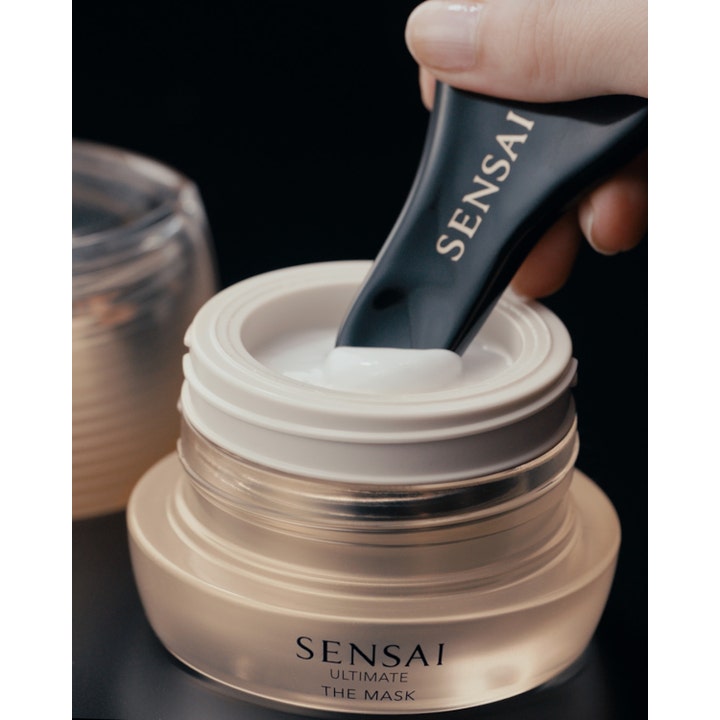 Sensai Ultimate The Mask 75 ml ansiktsmaske i gullfarget krukke med hvit kremet tekstur og svart spatel