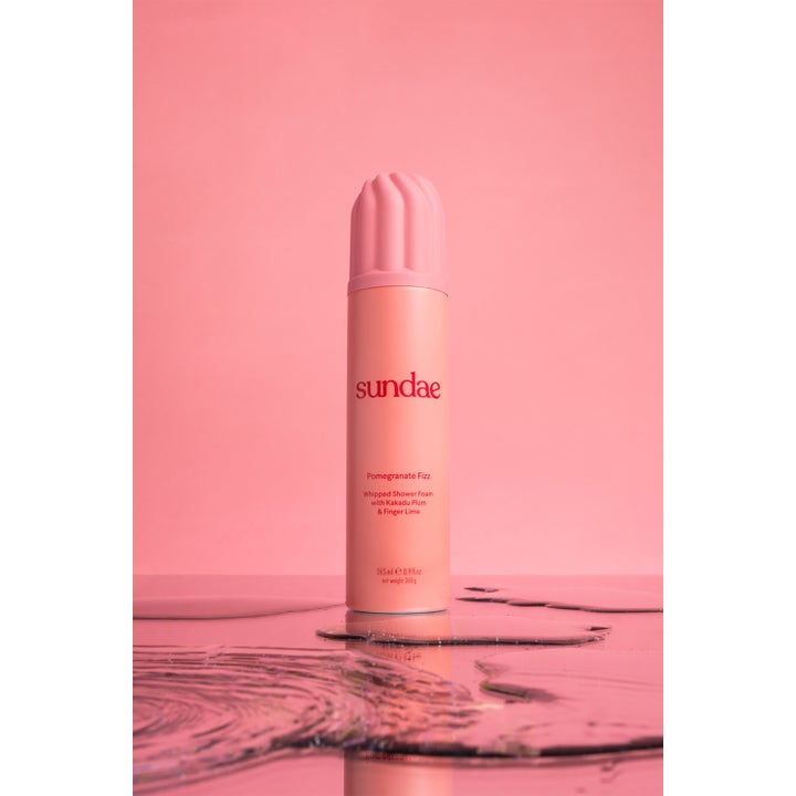 Sundae Whipped Shower Foam Pomegranate Fizz 265 ml dusjsåpe gir frisk kroppspleie i ferskenfarget flaske stående i vann.