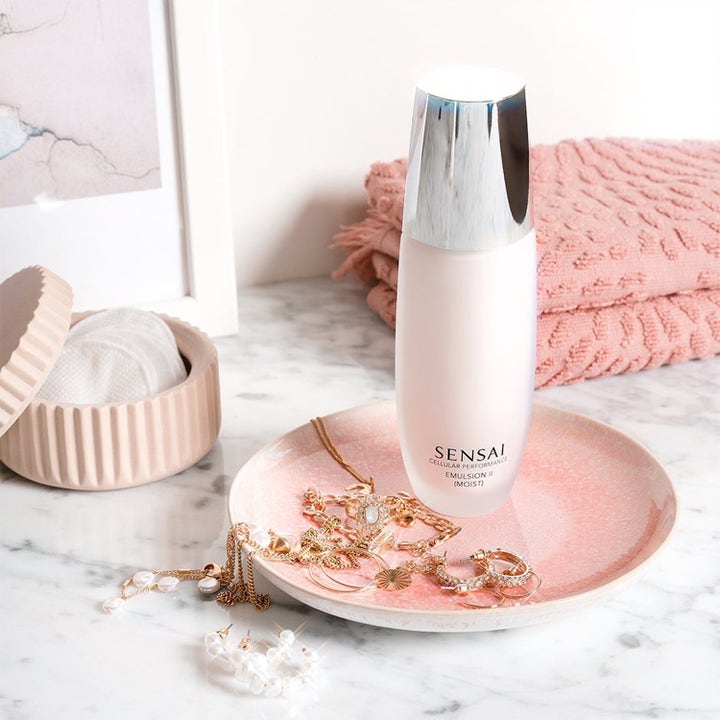 Sensai Moisture & Soap Cleanse fuktighetsgivende ansiktsemulsjon i hvit flaske med sølvlokk i et livsstilsmiljø
