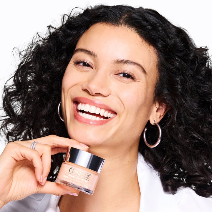 Clinique Moisture Surge Megastars fuktighetskrem i krukke som gir glød til smilende kvinne med mørkt hår