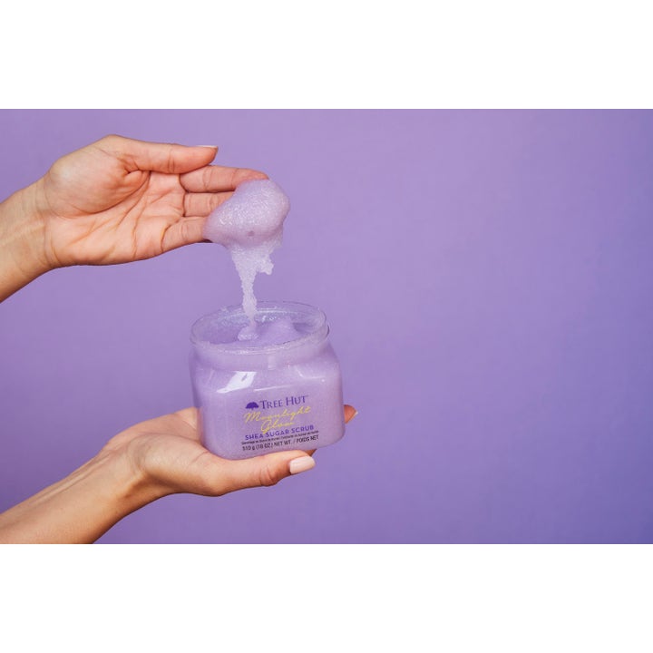 Tree Hut Shea Sugar Scrub Moonlight Glow 510 g kroppsskrubb med glitrende lilla tekstur som løftes ut av krukken.