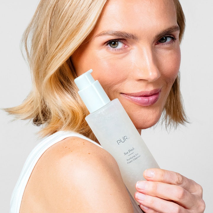 PÜR Sea Fresh Purifying Gel Foam Cleanser 150 ml rengjøringsgel i frostet pumpeflaske holdt av en smilende kvinne