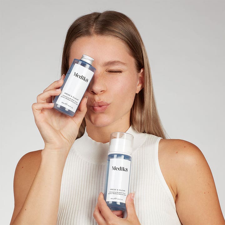 Medik8 Press & Clear 150 ml eksfolierende BHA toner i blå flasker med pumpe og skrukork holdt av kvinne