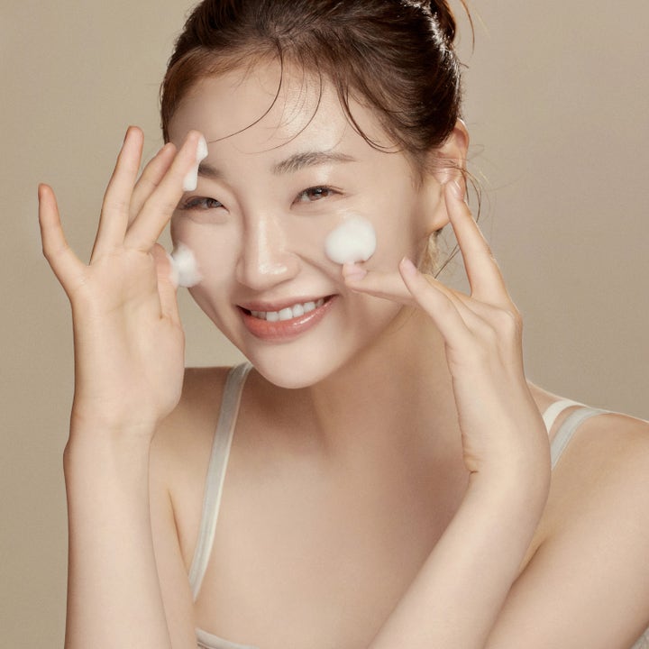 Hyggee All-In-One Care Cleansing Foam 150 ml rengjøringsskum som gir ren hud vist på en smilende kvinne med hvitt skum.
