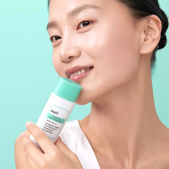 Klairs All-day Airy Mineral Sunscreen 60 g beroligende solkrem med SPF 50+ i hvit tube med mintgrønn kork holdt av kvinne.