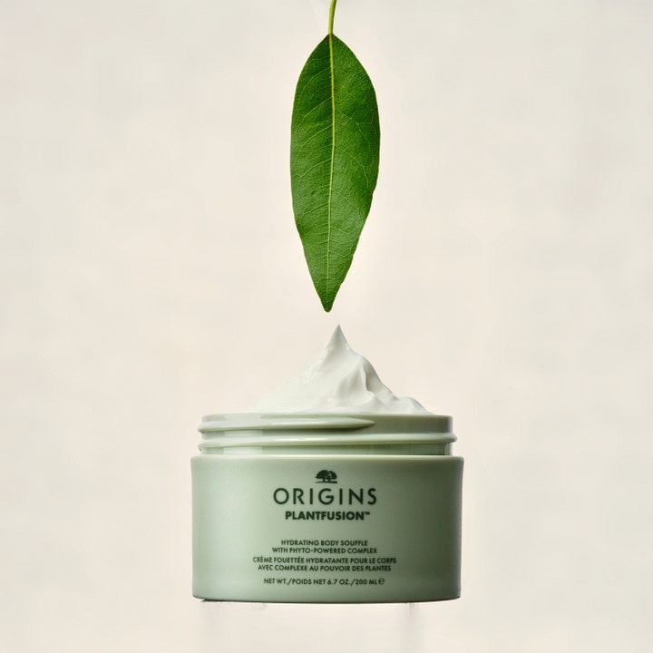 Origins Plantfusion Hydrating Body Souffle 200 ml fuktighetsgivende kroppskrem med hvit tekstur under et grønt blad.
