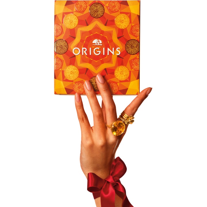 Origins Ginzing Glowing Essentials Set hudpleiesett med vitamin C for glød i oransje eske holdt av en hånd.