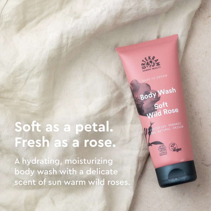 Urtekram Body Wash Soft Wild Rose 200 ml gir fuktighet i en rosa tube plassert på lyst linstoff.