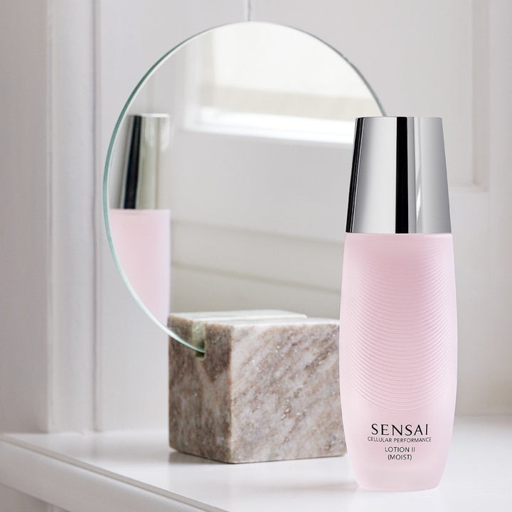 Sensai Cellular Performance Lotion II Moist fuktighetsgivende ansiktsvann i rosa flaske med sølvlokk ved et speil