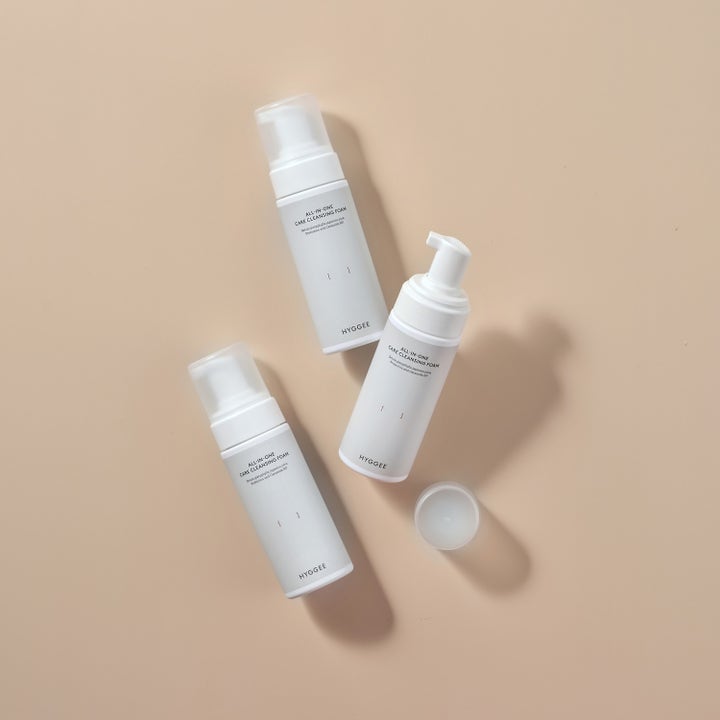 Hyggee All-In-One Care Cleansing Foam 150 ml ansiktsrens med ceramider i tre hvite pumpeflasker på beige bakgrunn.