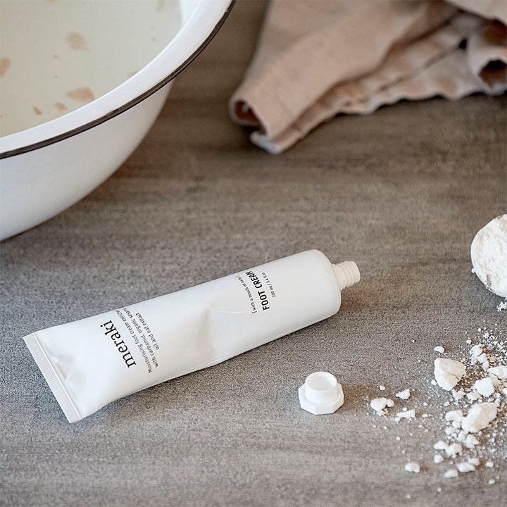 Meraki Foot Cream 100 ml fuktighetsgivende fotkrem i hvit tube ved siden av et hvitt fotbad og et håndkle.