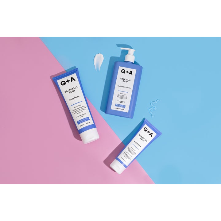 Q+A Salicylic Acid Body Wash 250 ml eksfolierende dusjsåpe i blå tube vist med lotion og geltekstur på farget bakgrunn.