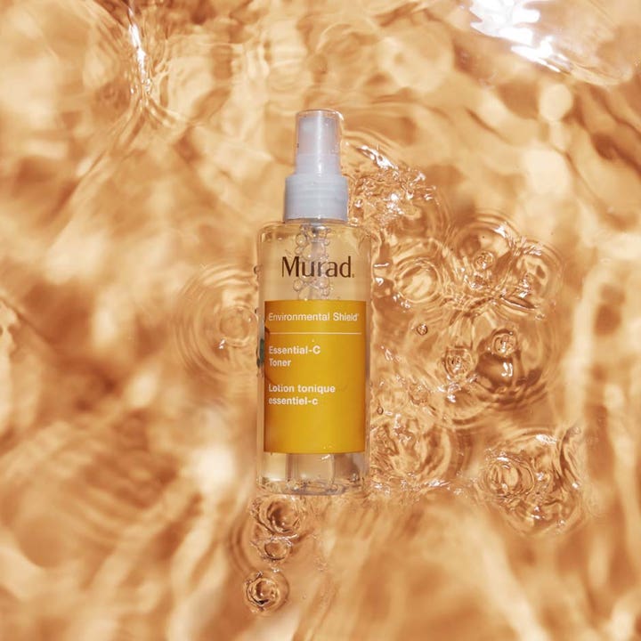 Murad Essential-C Toner 180 ml i en sprayflaske som flyter i vann med forfriskende gylne bølger.