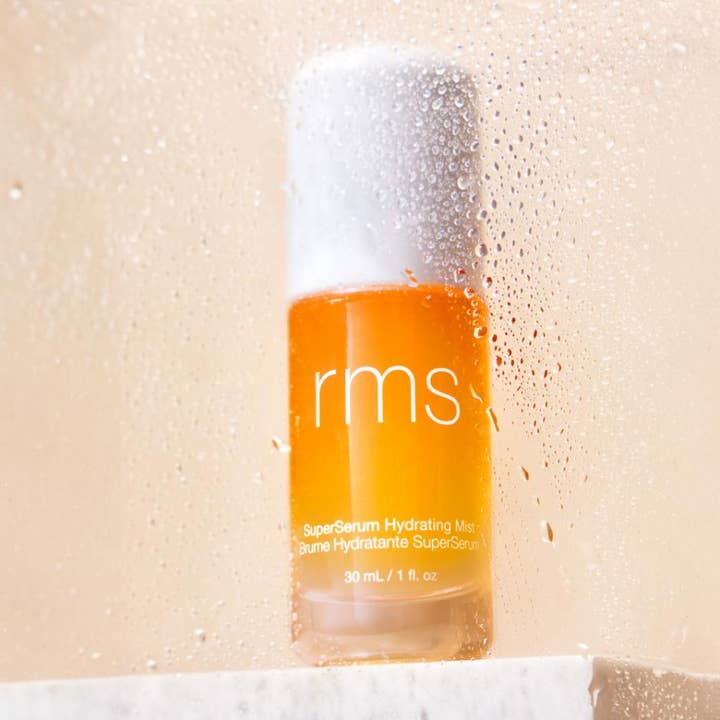 RMS Beauty SuperSerum Hydrating Mist 30 ml fuktighetsgivende ansiktsspray i en oransje flaske sett gjennom vanndråper