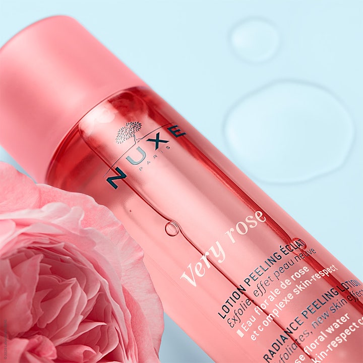 Nuxe Very Rose Peeling Lotion 150 ml eksfolierende peeling i rosa flaske ved siden av en stor rosa rose