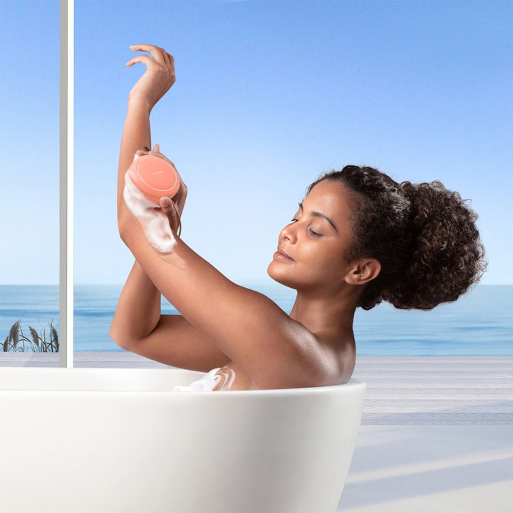 FOREO LUNA™ 4 body Peach Perfect 1 stk kroppsbørste gir glød og brukes av kvinne i badekar med skum og havutsikt