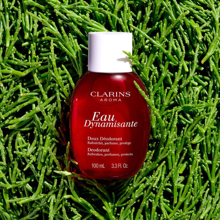 Clarins Eau Dynamisante Deodorant Spray 100 ml i rød glassflaske på en seng av grønne urter