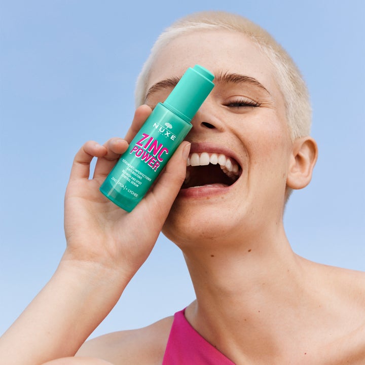 Nuxe Zinc Power 30 ml serum mot urenheter holdes av en smilende person mot en blå himmel