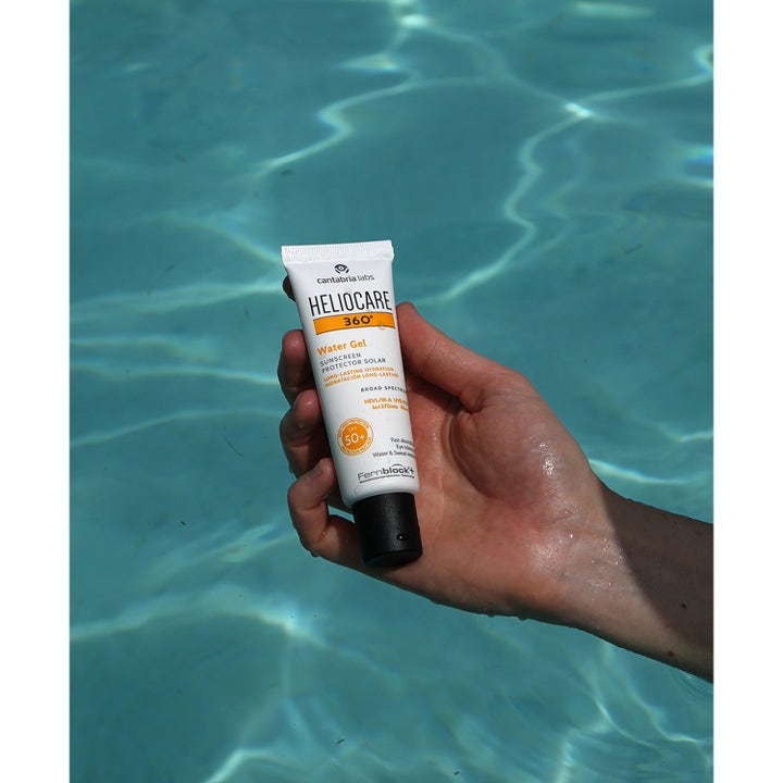 Heliocare 360 Watergel SPF 50+ 50 ml fuktighetsgivende solkrem i hvit tube holdes over et blått svømmebasseng
