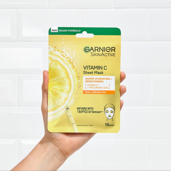 Garnier SkinActive Vitamin C Sheet Mask 28 g fuktighetsgivende maske i gul pakning som holdes mot en hvit vegg
