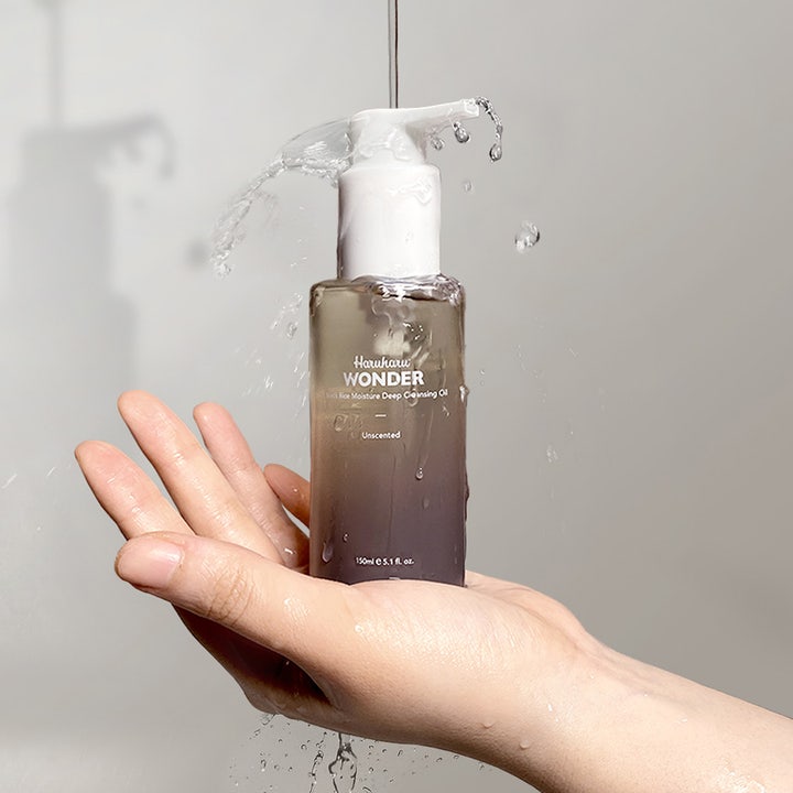 haruharu wonder Black Rice Moisture Deep Cleansing Oil 150 ml ansiktsrens i lilla flaske holdt i en hånd med vannsprut.