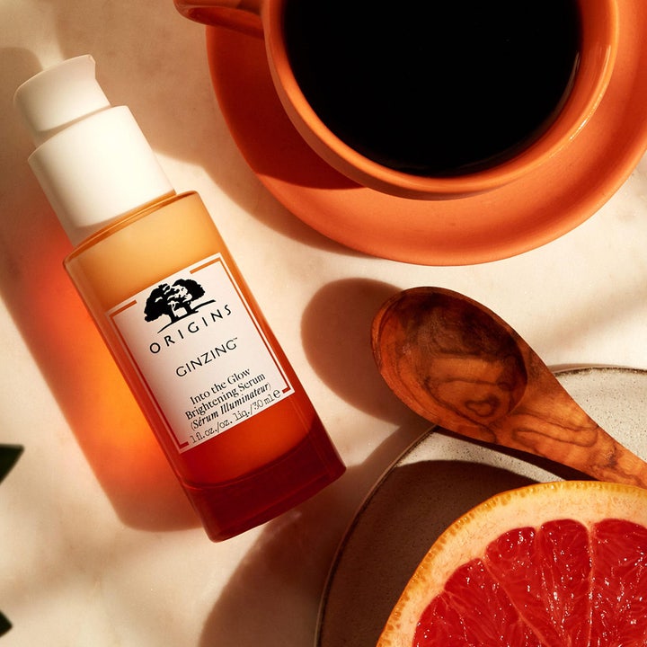 Origins GinZing Into the Glow Brightening Serum 30 ml ved siden av kaffe og grapefrukt som gir glød