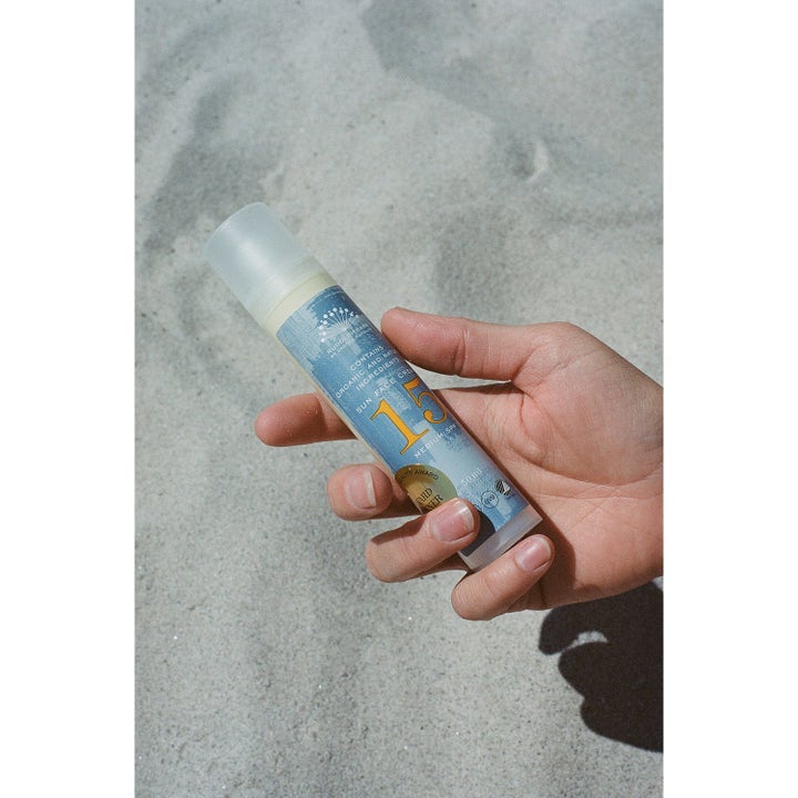 Rudolph Care Sun Face Cream 50 ml beskyttende solkrem ansikt SPF 15 i blå pumpeflaske holdt over lys sand.